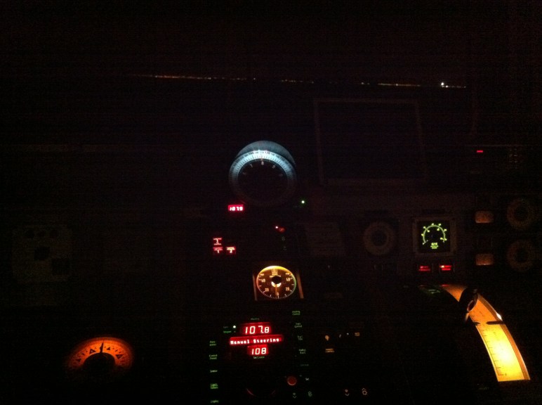 La consola del timonel, en el puente. Al fondo la línea de luces de la costa, en la que destaca en destello del faro de Chipiona.