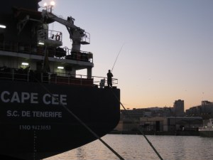 Un marinero pesca desde toldilla al amanecer.
