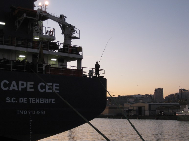 Un marinero pesca desde toldilla al amanecer.